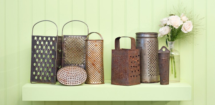 vintage cheese graters on a shelf next to a glass bottle of flowers