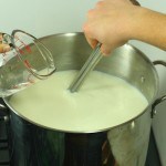 Diluted calcium chloride being poured into and stirred in pot of milk