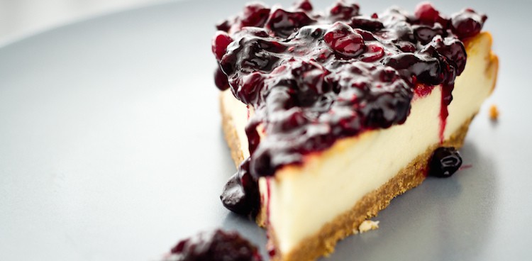 Wedge of cheesecake covered in cherries in sauce