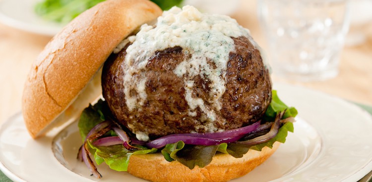 stock image of a large blue hamburger topped with melted blue cheese on a bed of red onions and lettuce on a bun