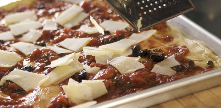 uncooked pizza with sauce and black olives with cheese being grated on top