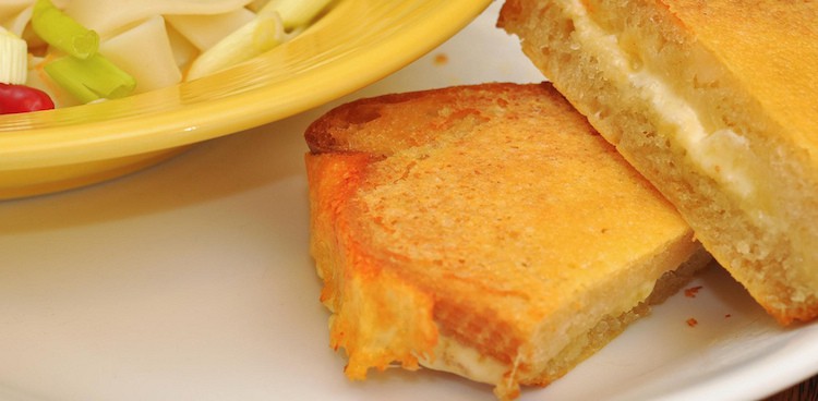 Plain grilled cheese sandwich cut into triangles on plate next to bowl of soup