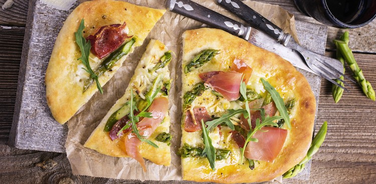 spring pizza with asparagus and prosciutto cut into pieces with rustic flatware