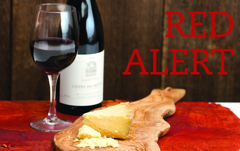 A bottle and glass of a Rhône red sit next to a cheeseplate.