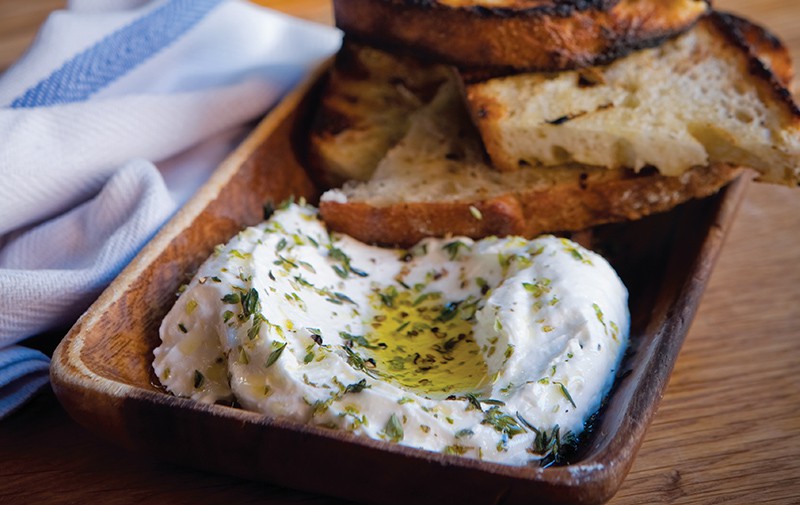 A thick, creamy spread of ricotta cheese features drizzled olive oil on top and toasted slices of bread for dipping goodness.