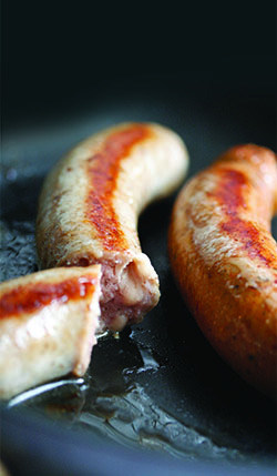 Three sausages sizzle in a cast-iron frying pan.