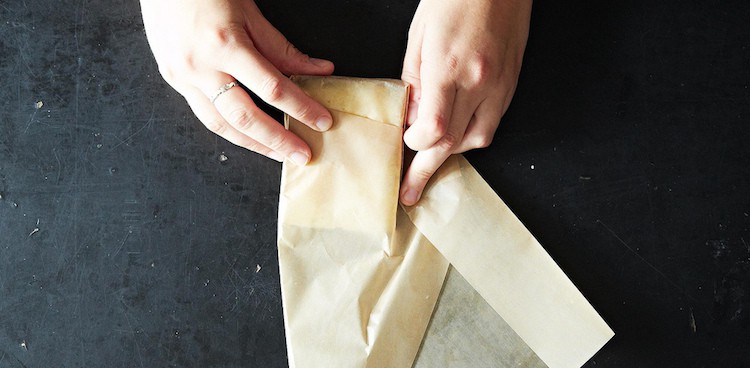 Two hands wrapping a wedge of cheese in plain brown paper