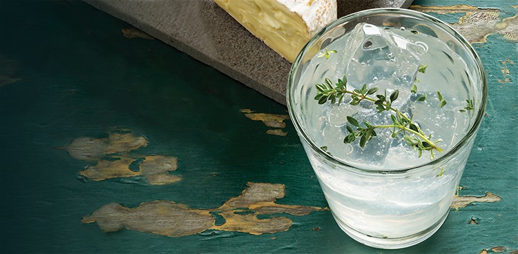 Gin fizz with a sprig of thyme in the glass and half wheel of Kunik on a slate