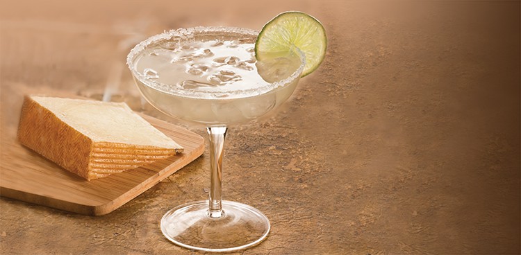 Margarita garnished with salt and lime with a slice of manchego in the background