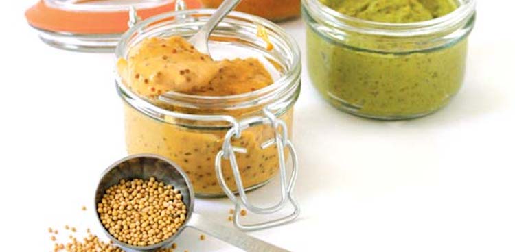 three flavored mustards in pots with mustard seeds spilling from measuring spoon in foreground