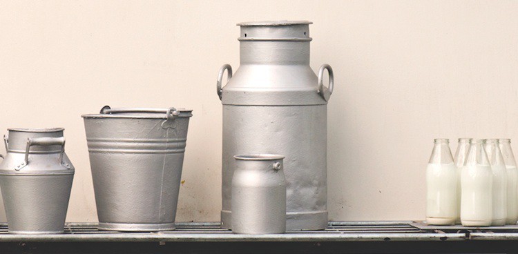 old fashioned silver milk jugs and pails stand on a table next to glass milk bottles