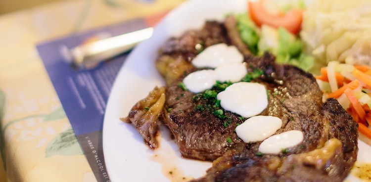 A charred steak next to a ball of herb butter and julienned vegetables, topped with Epoisses sauce