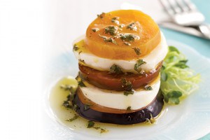 Fresh mozzarella stacked into towers with slices of plum and kumato tomato and golden beet and drizzled with herb vinaigrette