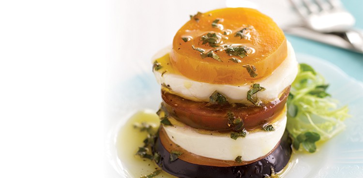 Fresh mozzarella stacked into towers with slices of plum and kumato tomato and golden beet and drizzled with herb vinaigrette