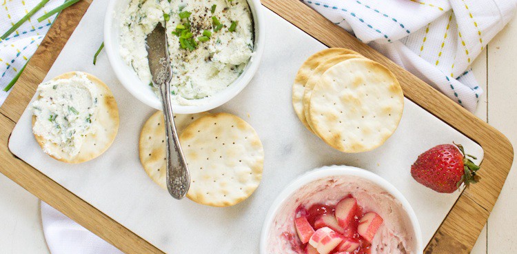 Beauty shot of two containers of homemade cream cheese, one flavored with black pepper and fresh chives, the other with strawberry syrup and fresh rhubarb