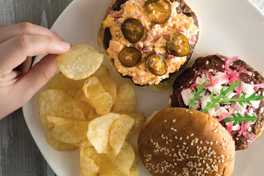 a plate with a burger topped with pimento cheese and a lamb burger topped with feta and candied red onions