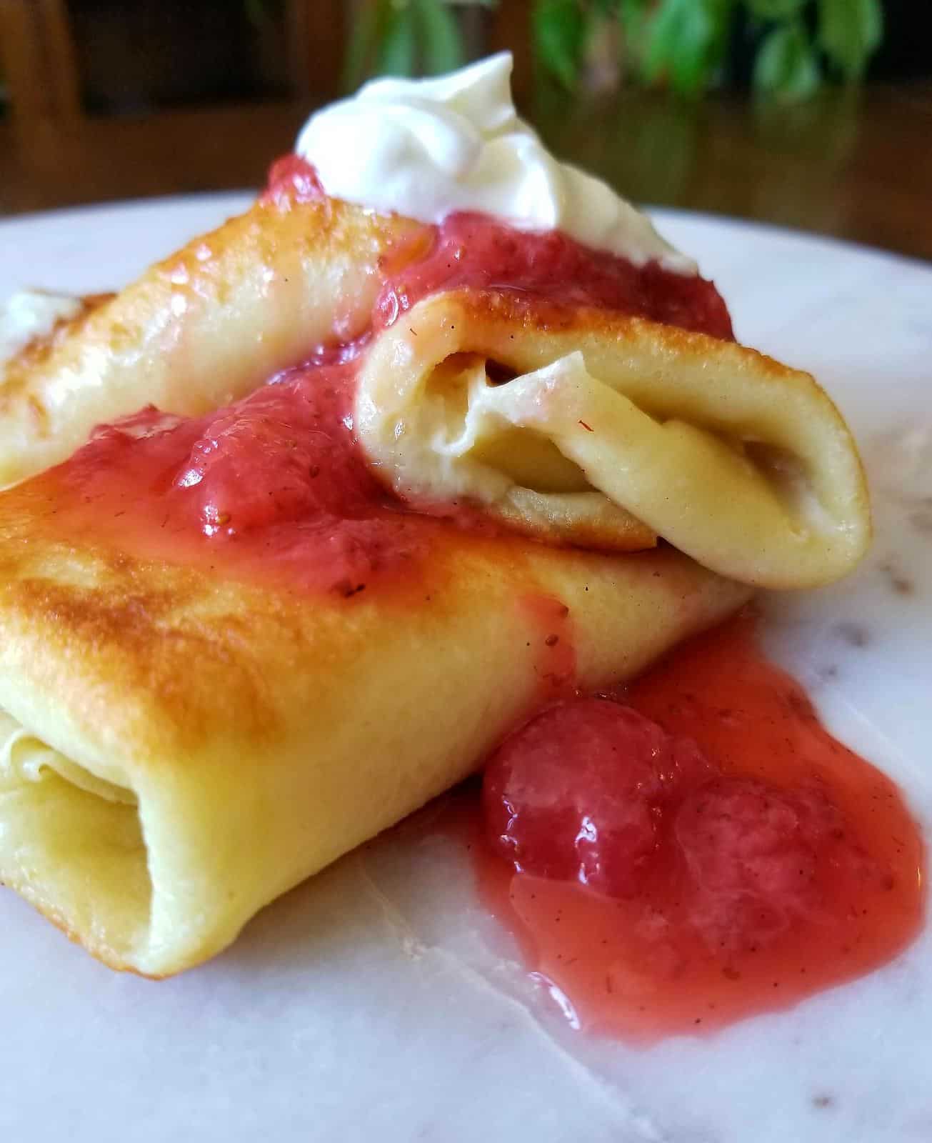 a plate of cheese blintzes stuffed with ricotta and culture sour cream and topped with strawberries