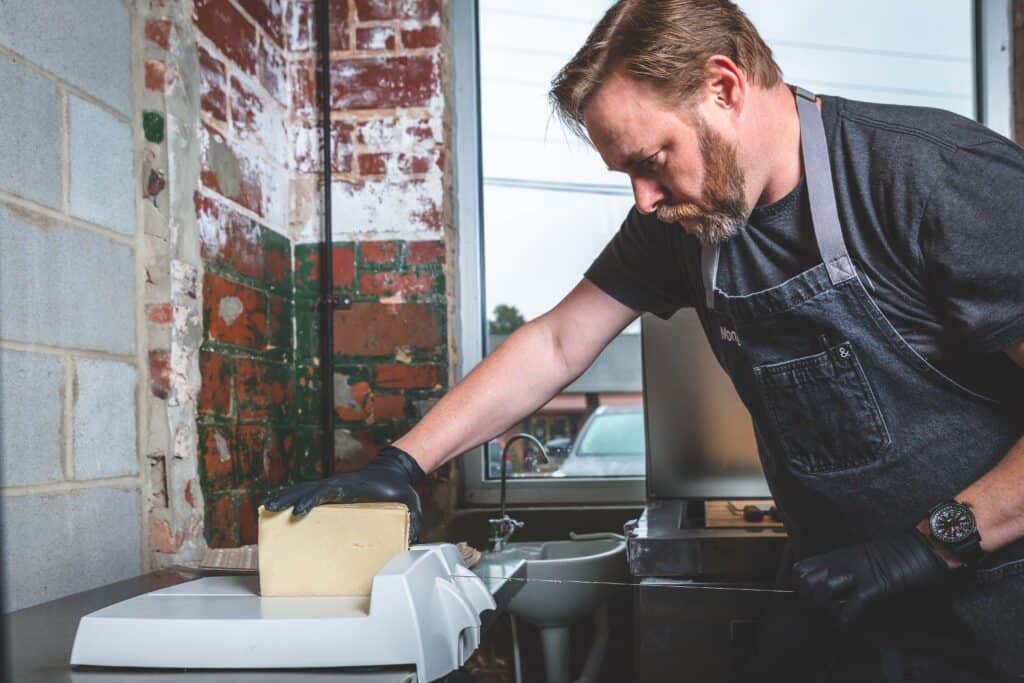 Stevie Webb, owner of the Cheese Shop in Carrboro, North Carolina, cuts a block of cheese in his shop. 