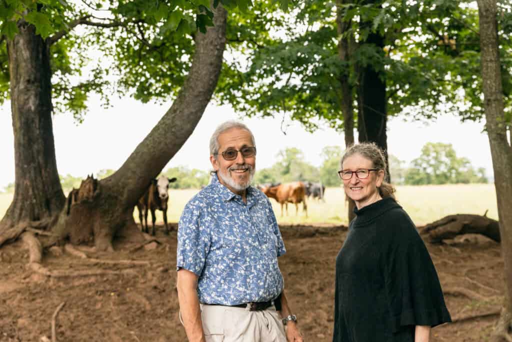 Jonathan and Nina White, the owners of Bobolink Dairy, look at the camera as cows graze in the foreground.