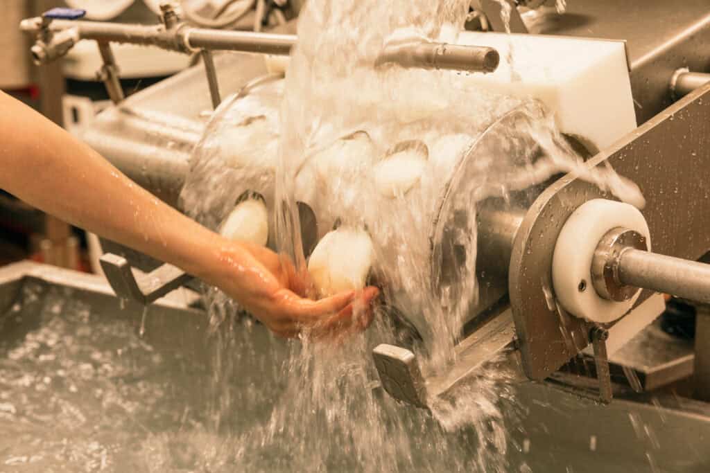 A hand catches mozzarella balls under lots of rushing water.