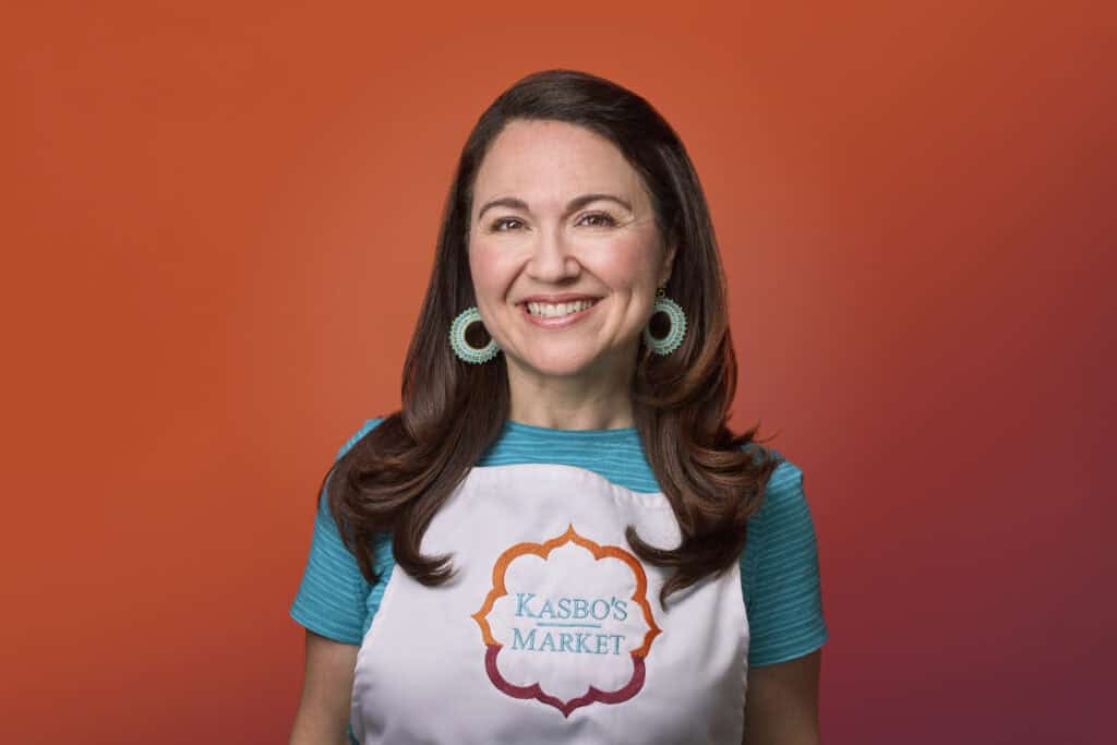 Smiling woman with dark hair and an apron that says, "Kasbo's Market." 