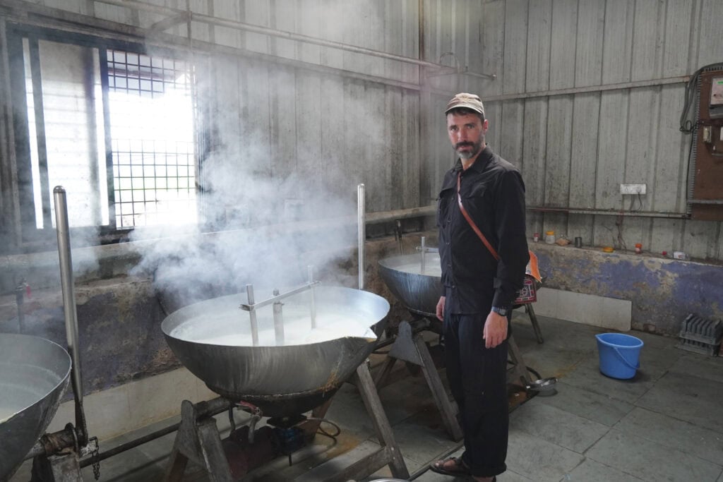 A man with a beard standing over a vat of steaming milk.