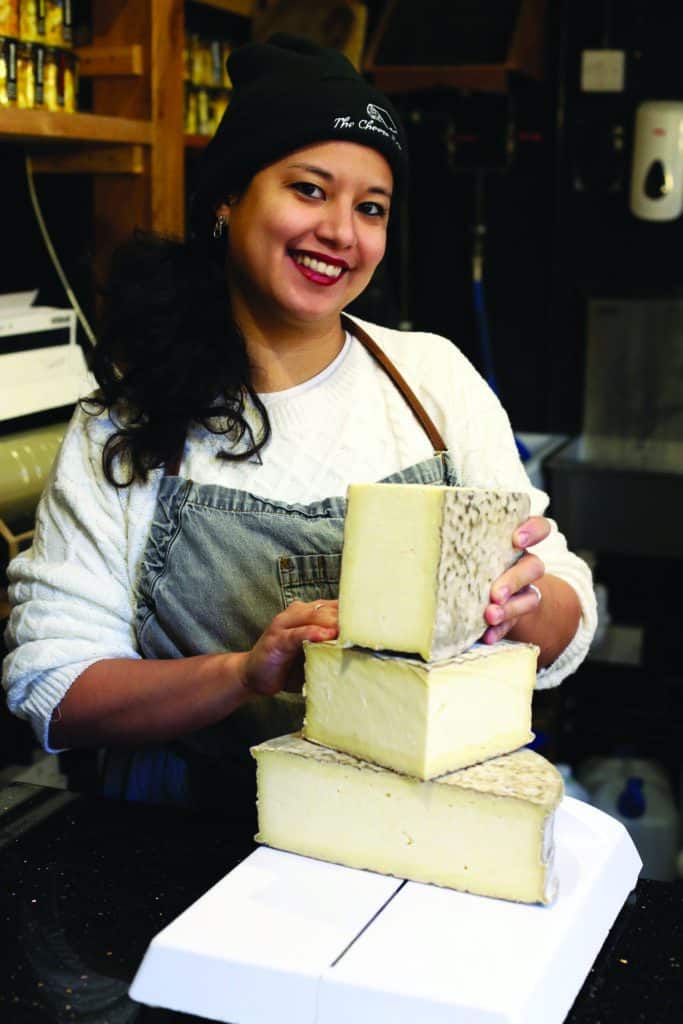 A woman smiles with blocks of cheese.