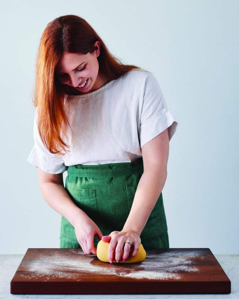 A woman kneads pasta dough.